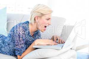Pretty blonde woman lying on the couch and using her laptop