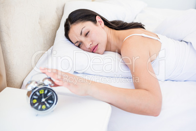 Pretty brunette turning off alarm clock on bed