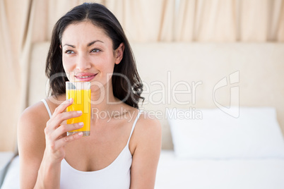 Pretty brunette holding a glass of orange juice on bed