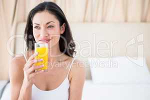Pretty brunette holding a glass of orange juice on bed