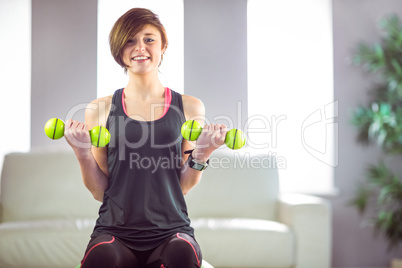 Fit woman lifting dumbbell sitting on ball