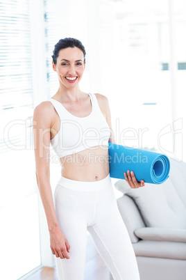 Smiling brunette holding exercise mat