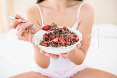 Pretty brunette holding a cereal bowl on bed