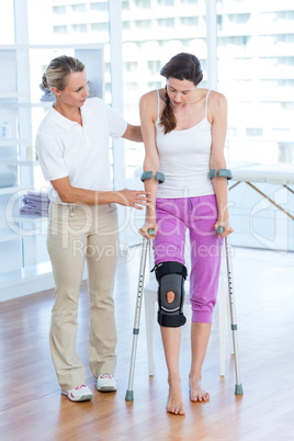 Doctor helping woman walking with crutches