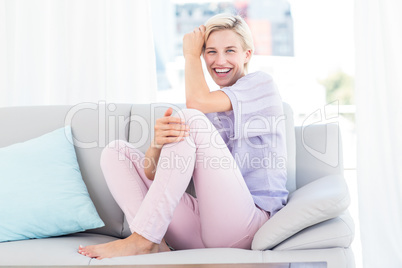 Pretty blonde woman sitting on the couch and smiling at the came Pretty blonde woman sitting on the couch and smiling at the came