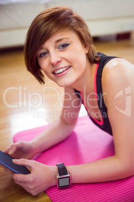 Fit woman looking at camera and using tablet pc on mat