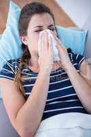 Sick woman blowing her nose lying on couch