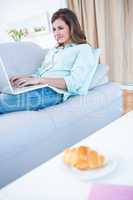 Happy brunette using her laptop on couch