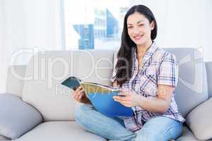 Pretty brunette looking at camera and holding a magazine on couc