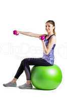 Fit woman lifting dumbbell sitting on ball