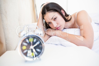 Pretty brunette watching alarm clock on bed