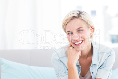Pretty blonde woman sitting on the couch and smiling at the came Pretty blonde woman sitting on the couch and smiling at the came