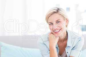 Pretty blonde woman sitting on the couch and smiling at the came
