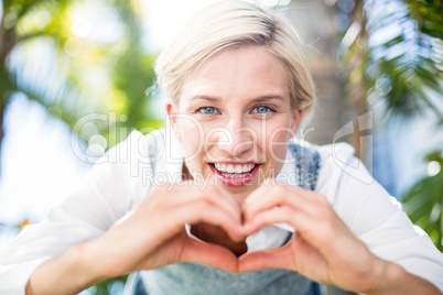 Pretty blonde woman smiling at the camera and doing heart shape