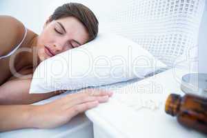 Woman sleeping in bed by spilt bottle of pills