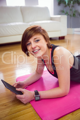 Fit woman looking at camera and using tablet pc on mat