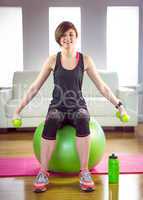 Fit woman lifting dumbbell sitting on ball