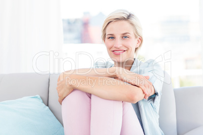 Pretty blonde woman sitting on the couch and smiling at the came Pretty blonde woman sitting on the couch and smiling at the came