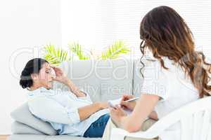 Depressed woman lying on the couch while her therapist taking no