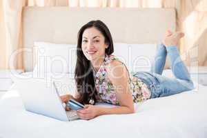 Pretty brunette looking at camera and shopping online on bed