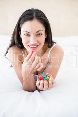 Pretty brunette eating candies on bed