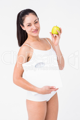 Smiling brunette holding weighing scales and apple