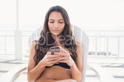 Pretty brunette sitting on a chair and texting with her mobile p