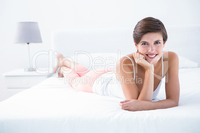 Happy brunette smiling at camera lying on bed