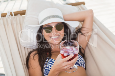 Pretty brunette relaxing on a hammock and drinking cocktail