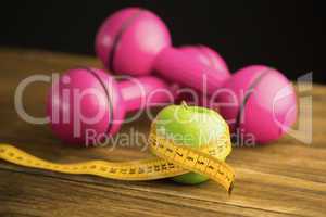 Pink dumbbells with green apple and measuring tape