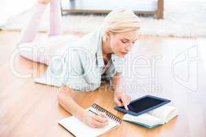 Pretty blonde woman lying on the floor and taking notes while us