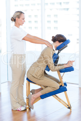 Businesswoman having back massage while using her mobile phone