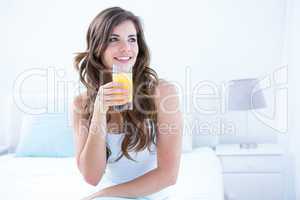Thoughtful brunette drinking a glass of orange juice