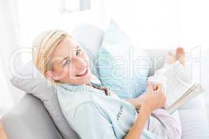 Pretty blonde woman reading a book and holding a mug