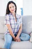 Pretty brunette looking at camera and smiling on couch