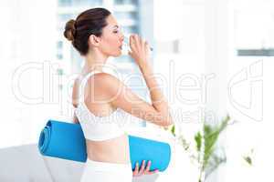 Brunette drinking water while holding exercise mat