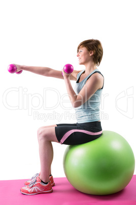 Pretty brunette exercising with dumbbells on fitness ball