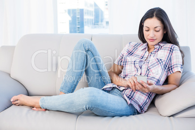 Pretty brunette lying on couch and using smartphone