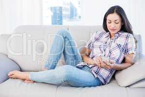 Pretty brunette lying on couch and using smartphone