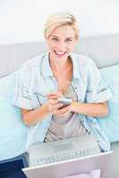 Pretty blonde woman using her laptop and texting with her mobile