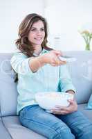 Happy brunette watching television with bowl of popcorn