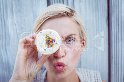 Pretty blonde woman grimacing with cupcake