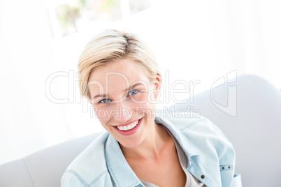 Pretty blonde woman sitting on the couch and smiling at the came