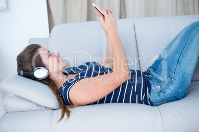 Pretty brunette listening music on couch with smartphone