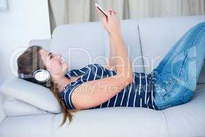 Pretty brunette listening music on couch with smartphone