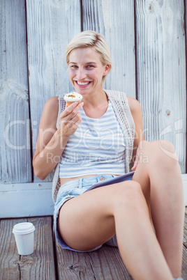 Pretty blonde woman holding cupcake and using her tablet