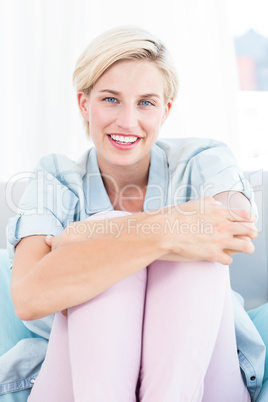 Pretty blonde woman sitting on the couch and smiling at the came Pretty blonde woman sitting on the couch and smiling at the came