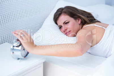 Pretty woman extending hand to alarm clock in bed