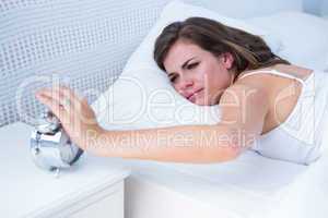 Pretty woman extending hand to alarm clock in bed