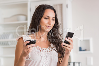 Pretty brunette using smartphone and having glass of wine